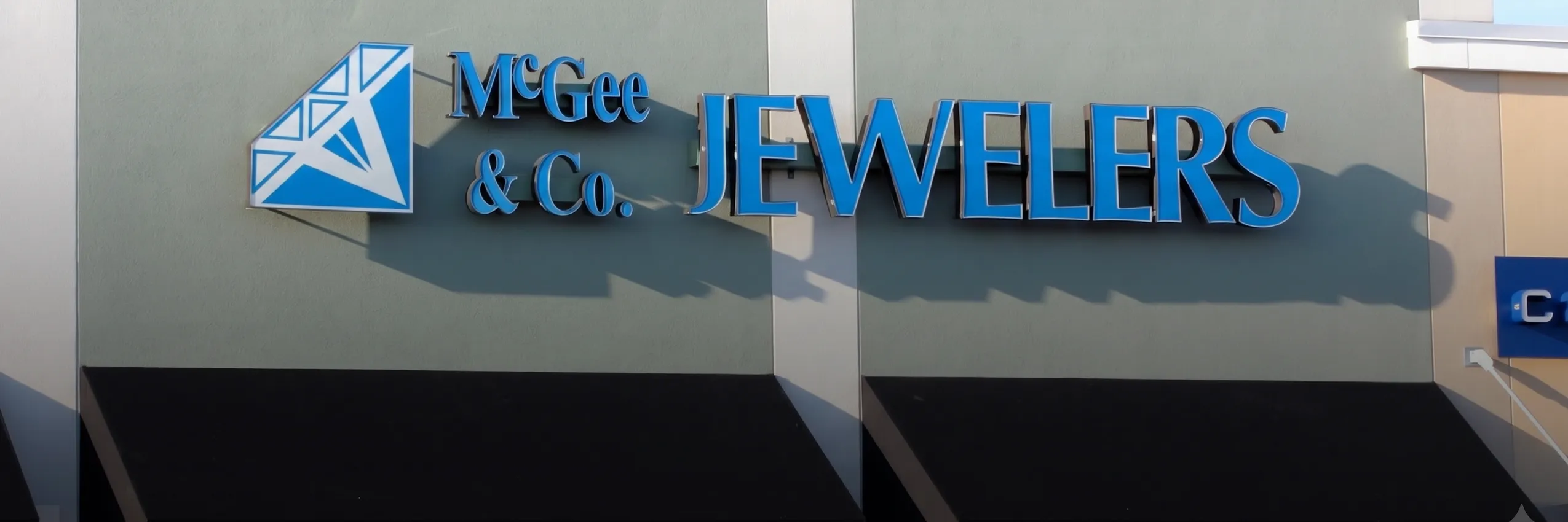 Storefront sign for McGee & Co. Jewelers with blue lettering and a diamond logo. Click to view store information.