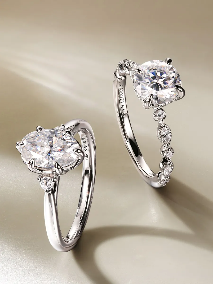 Elegant diamond engagement rings displayed on a reflective surface.