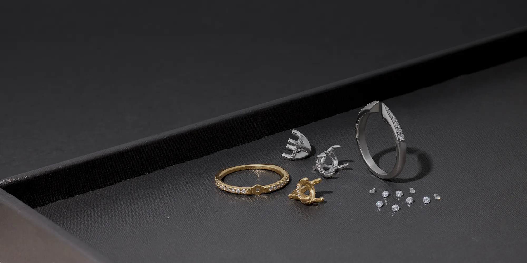 Custom engagement ring components and loose diamonds displayed on a dark surface.