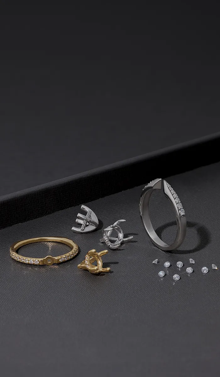 Custom engagement ring components and loose diamonds displayed on a dark surface.