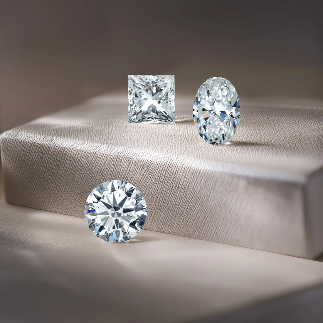 Three sparkling diamonds in different cuts on a textured surface.