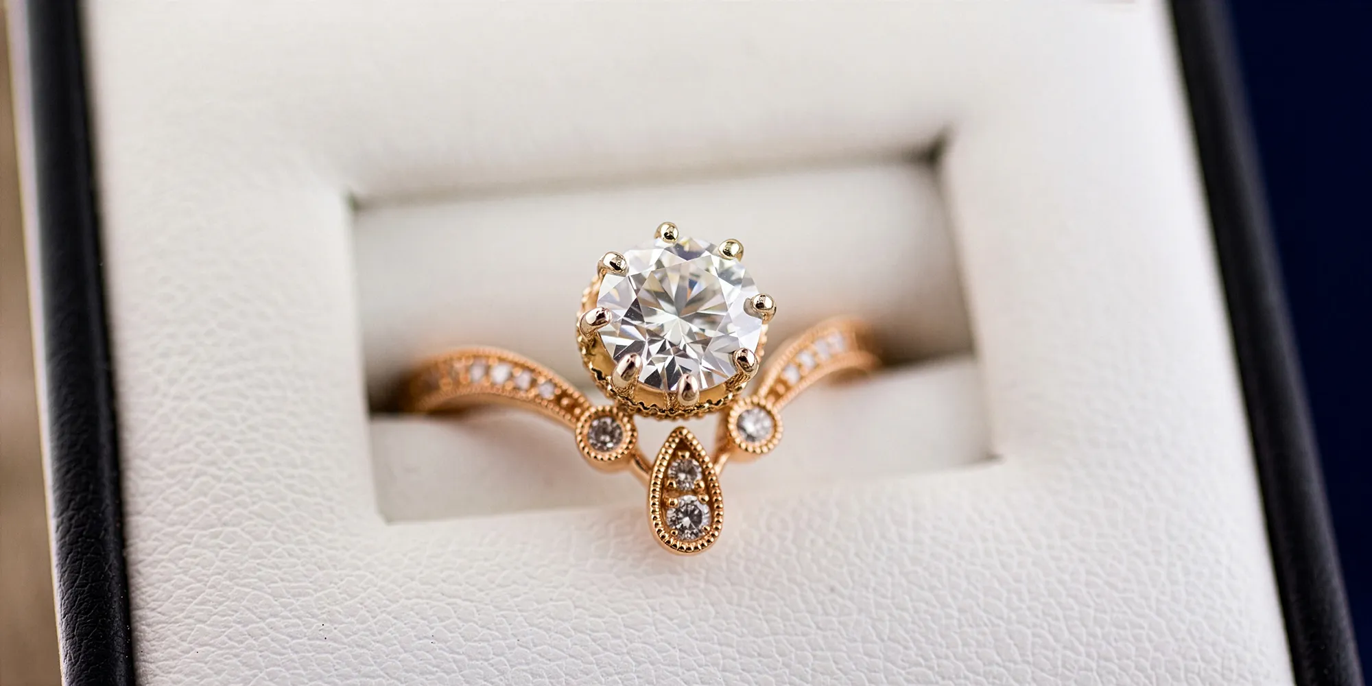 A rose gold engagement ring with a large diamond and intricate detailing in a jewelry box.