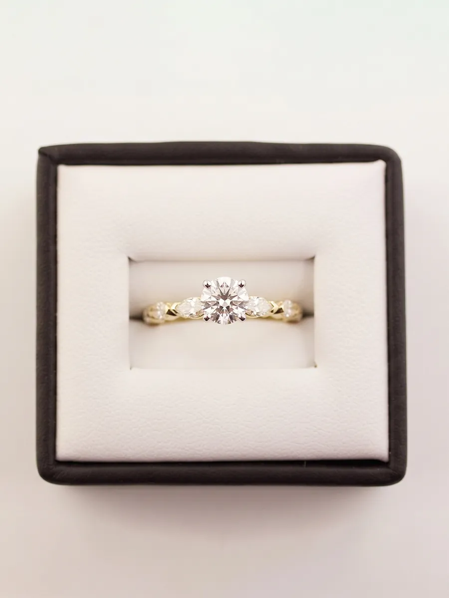 A gold engagement ring with a diamond in a black and white box.