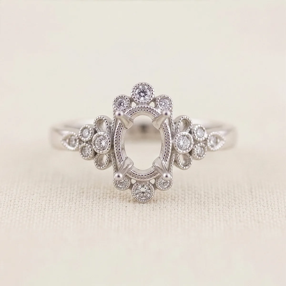 Ornate silver ring setting with intricate diamond accents on a neutral background.