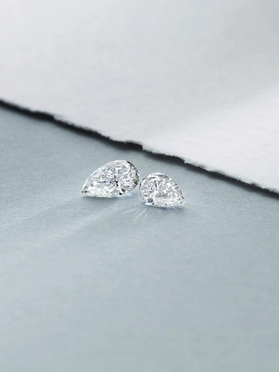 Two pear-shaped diamonds on a textured surface, showcasing their brilliance.