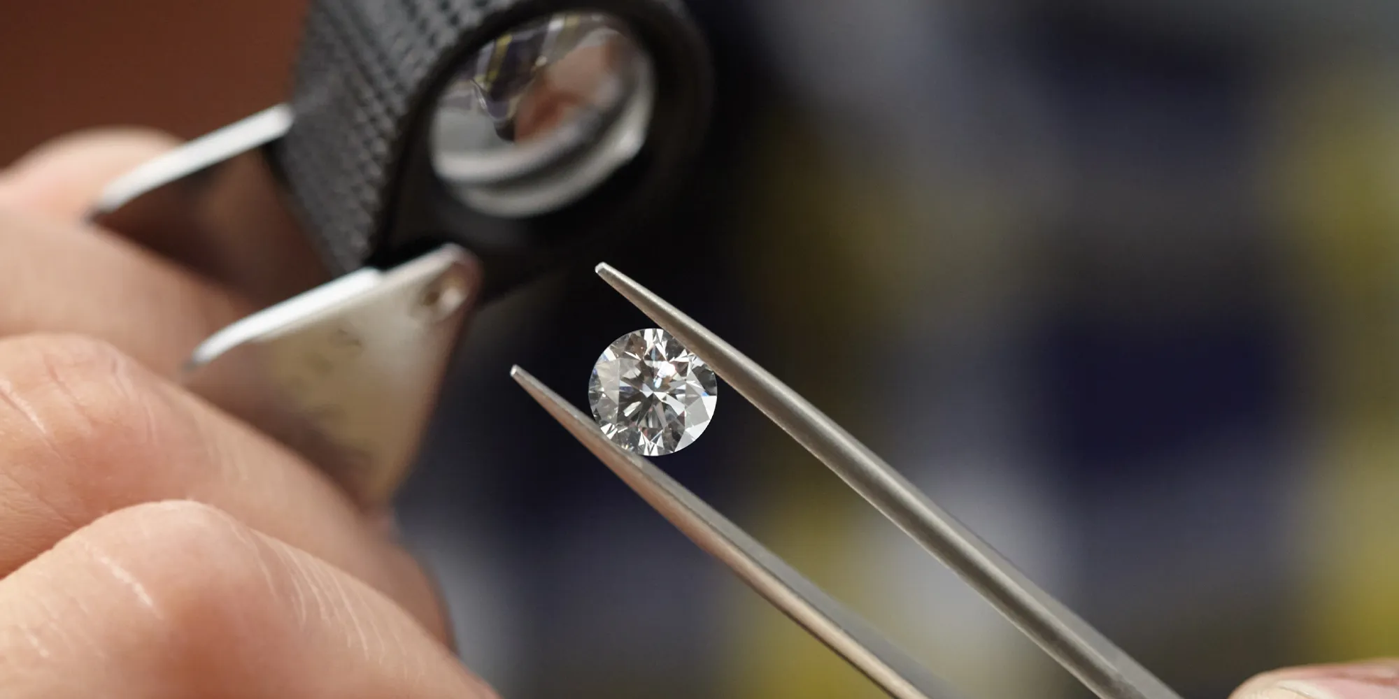 A diamond held by tweezers is examined with a magnifying glass.