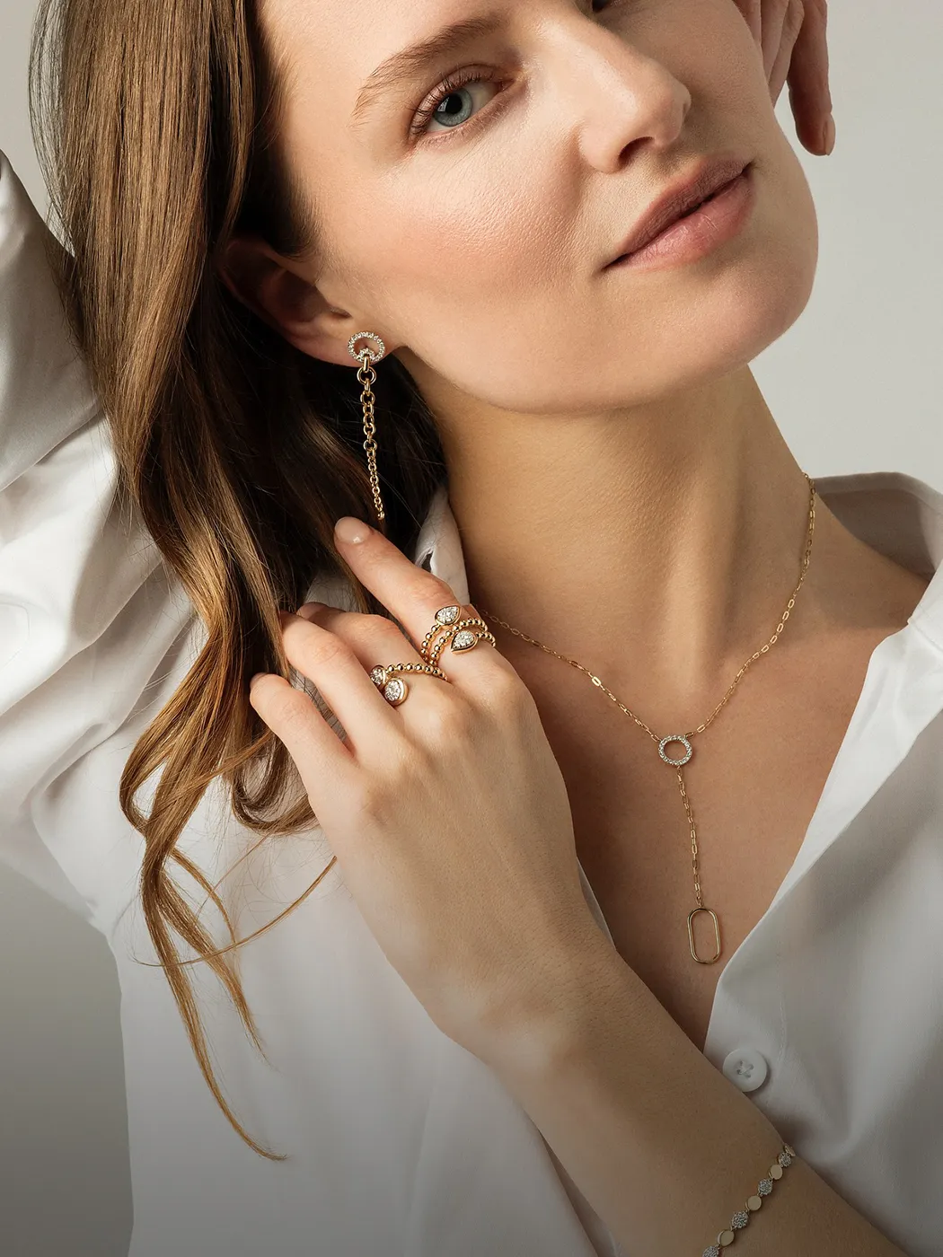 Woman wearing gold jewelry, including earrings, rings, and a necklace, with a white shirt.
