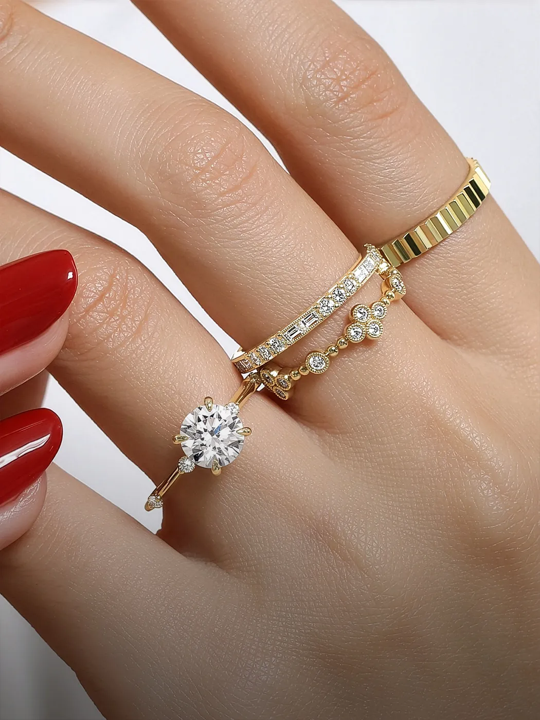 Hand with red nails wearing three gold rings, one with a large diamond.