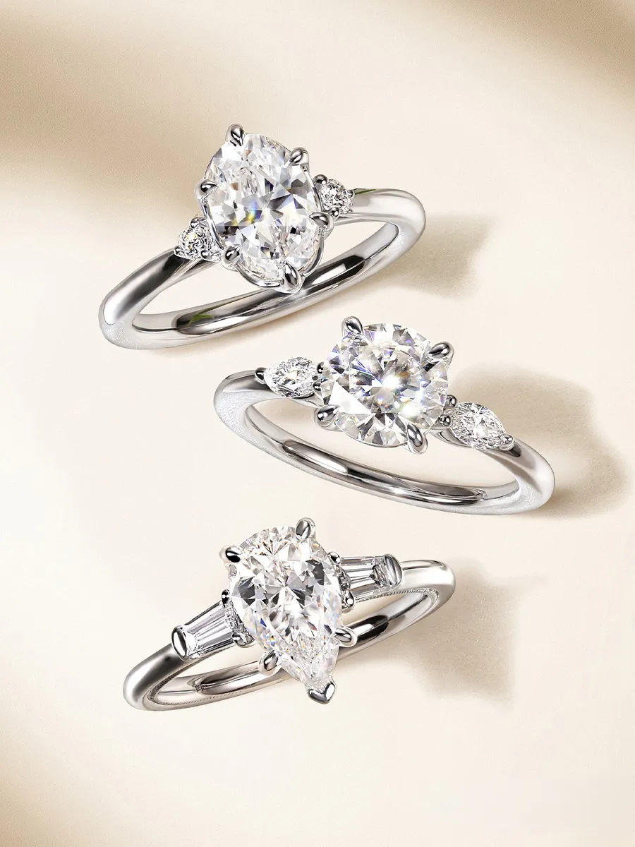 Three elegant diamond engagement rings with different cuts on a light background.