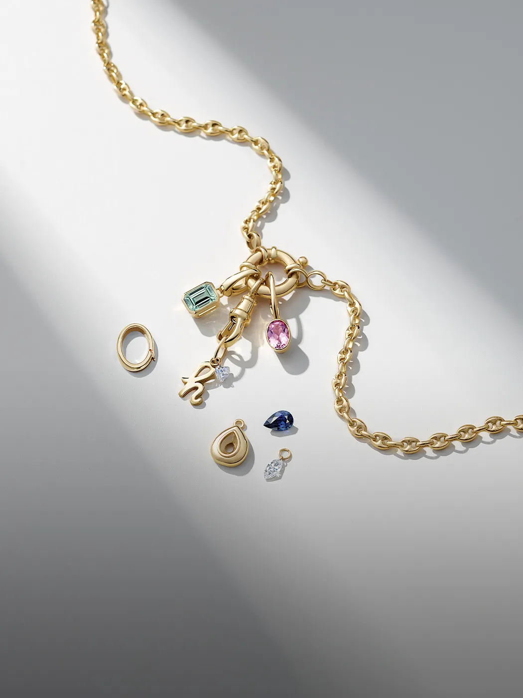 Gold chain with various charms and gemstones on a gray background.