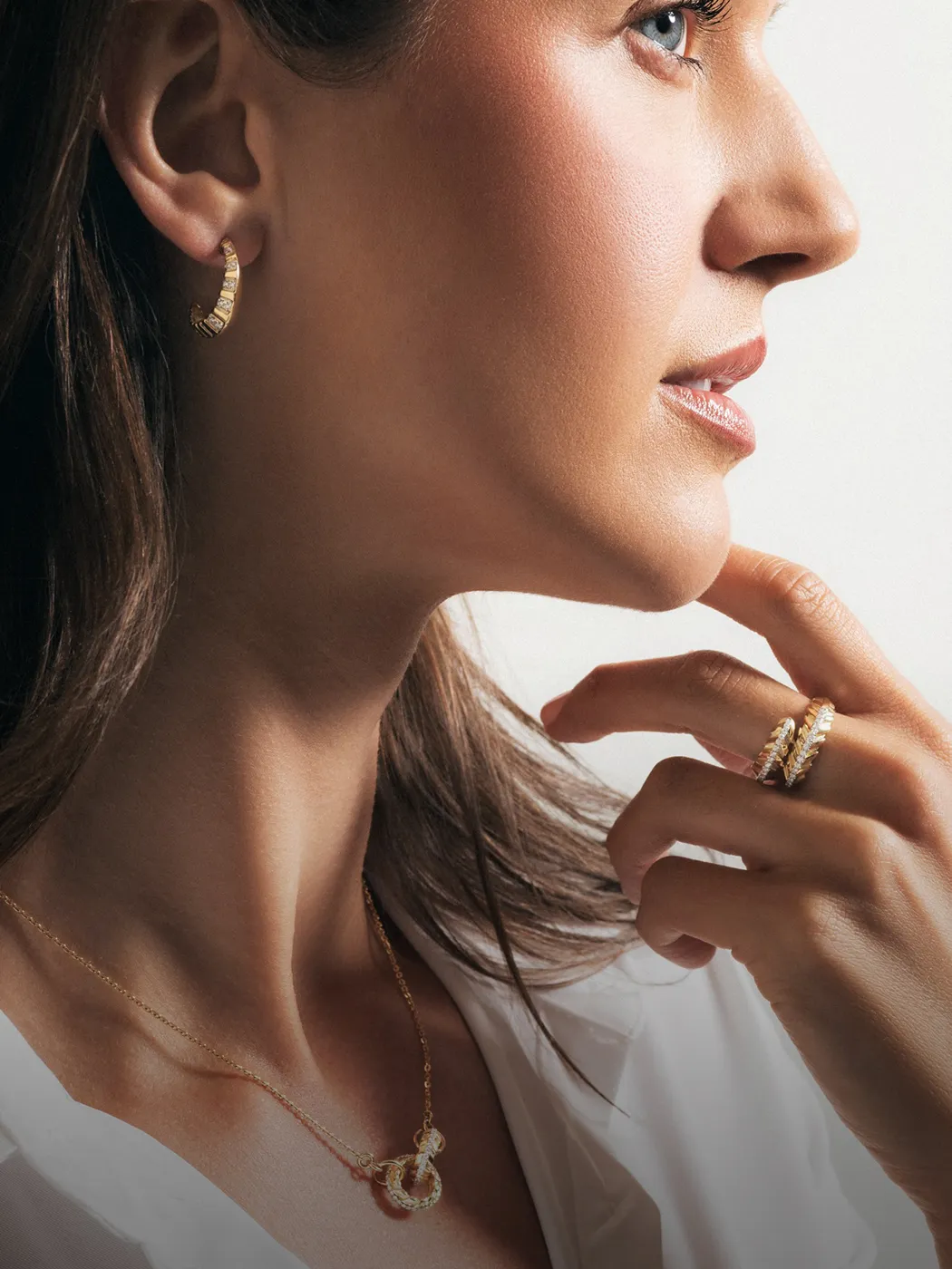 Woman wearing gold jewelry: earrings, necklace, and rings.
