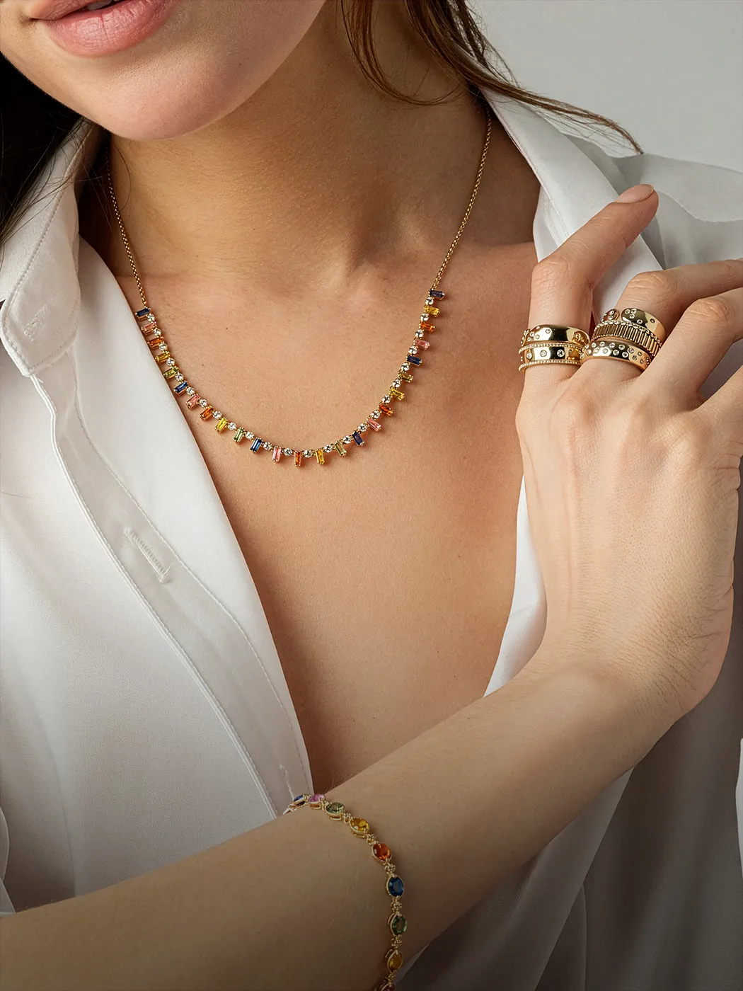 Woman wearing colorful gemstone necklace, bracelet, and rings.