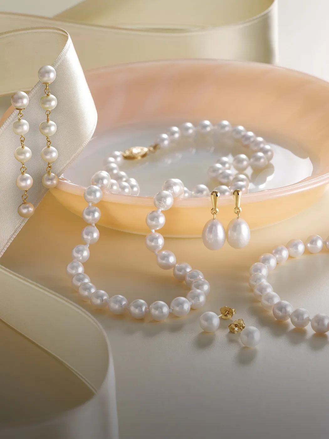Pearl necklace, bracelet, and earrings displayed with ribbon on a soft background.