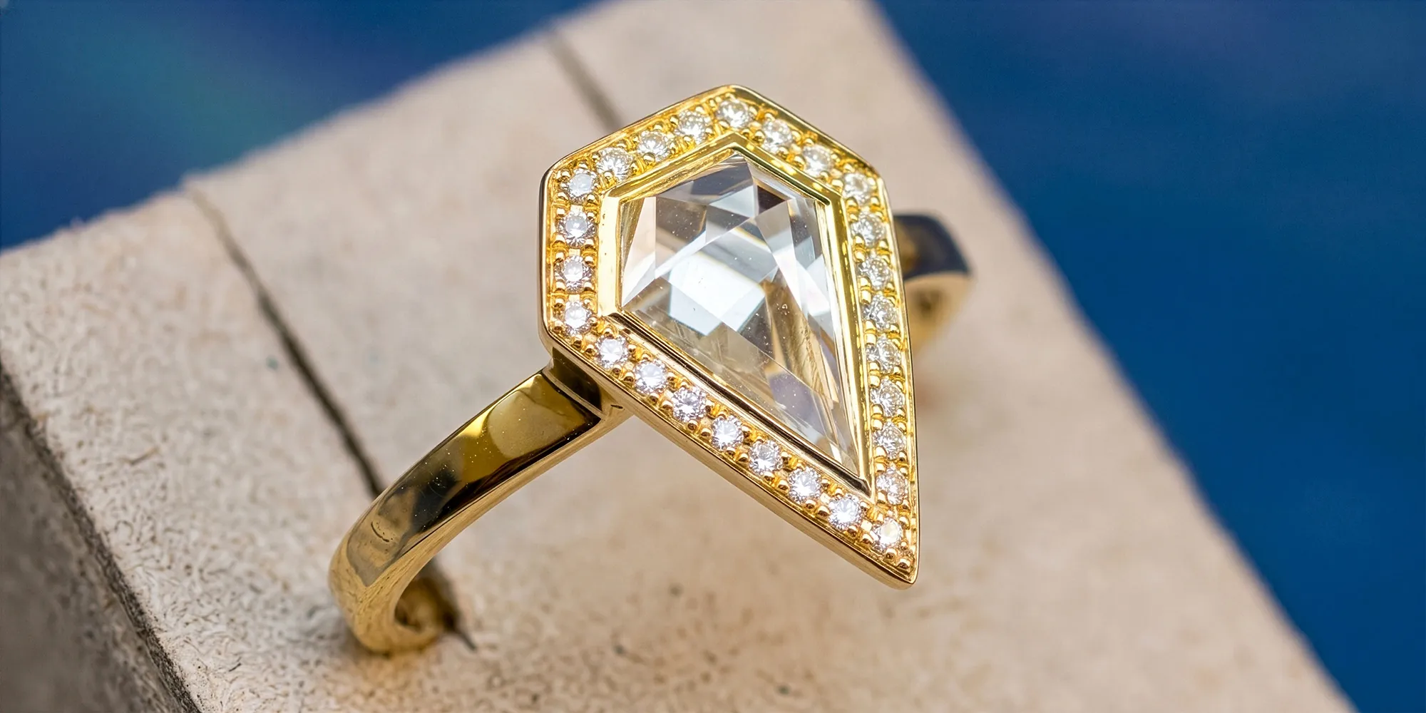 Gold ring with a geometric diamond surrounded by smaller diamonds on a textured surface.