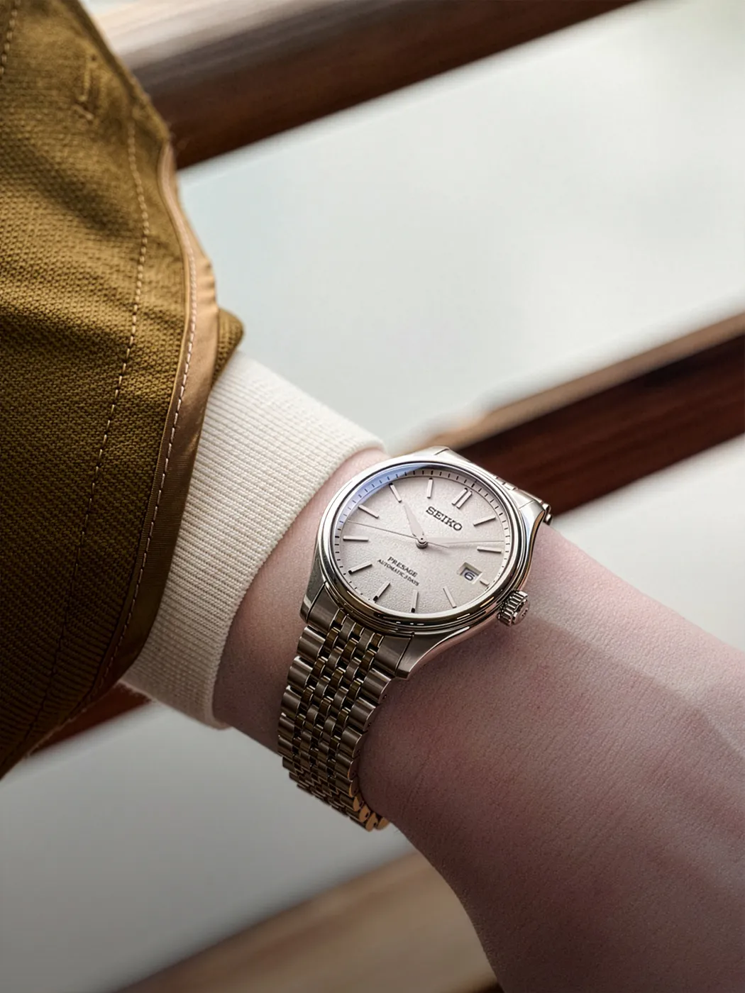 A wrist wearing a Seiko watch with a silver bracelet and white dial.
