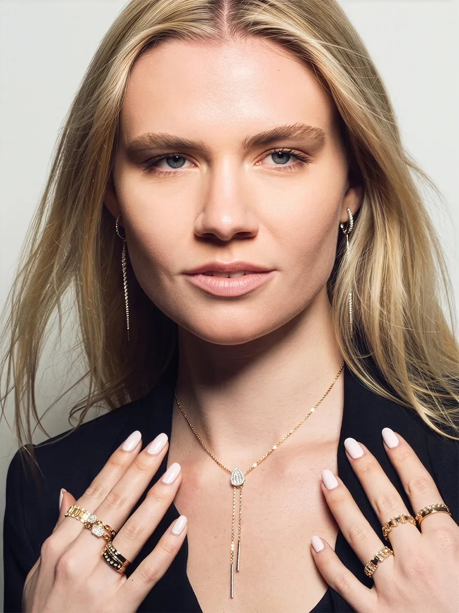 Woman wearing gold jewelry, including rings, necklace, and earrings, with a confident expression.