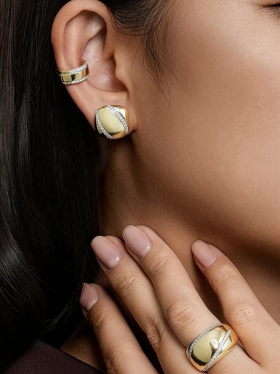 Close-up of a woman's ear and hand adorned with gold and diamond jewelry.