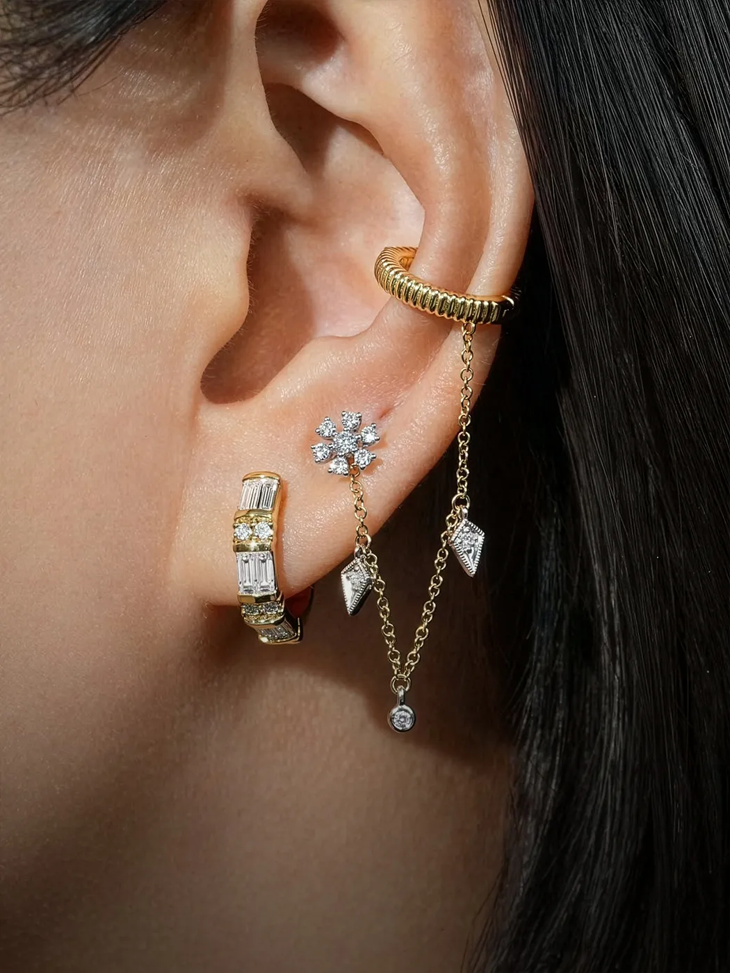 Elegant ear with multiple gold and diamond earrings, including a chain and cuff.