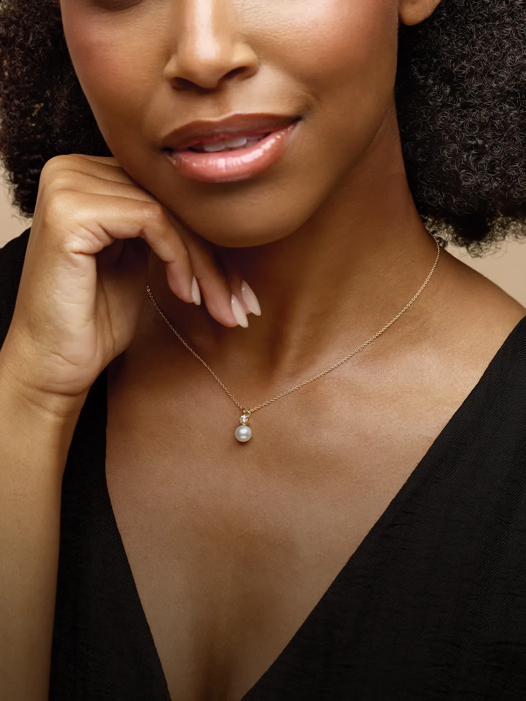 Woman wearing a pearl necklace, hand near chin, in a black top. Explore pearl jewelry at McGee & Company.