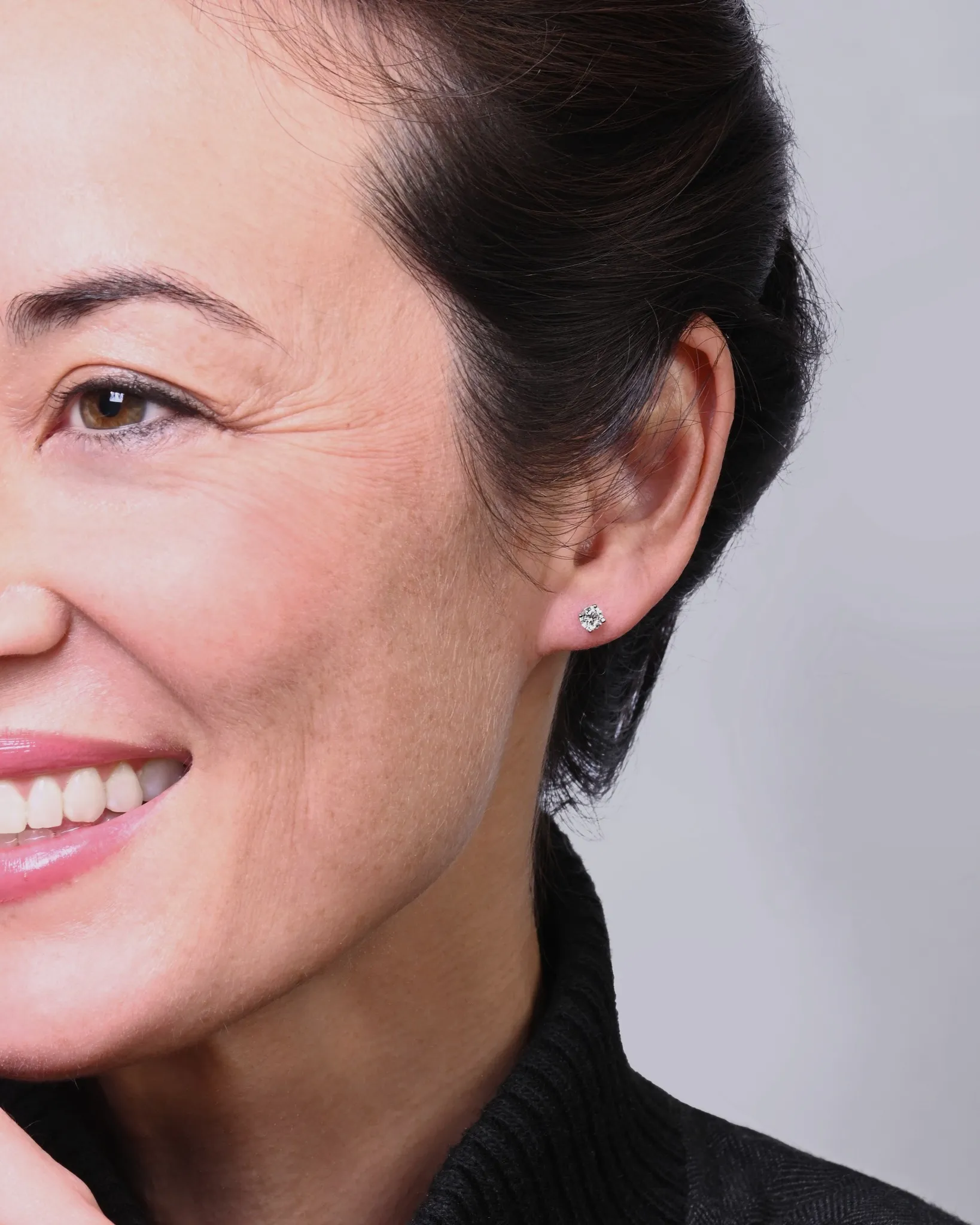 Woman smiling, wearing diamond stud earrings. Click to shop natural diamond studs at Michael & Son's Jewelers.