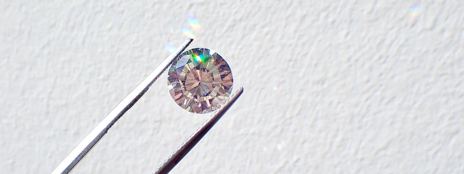 A close-up of a sparkling loose diamond held by tweezers against a light background.