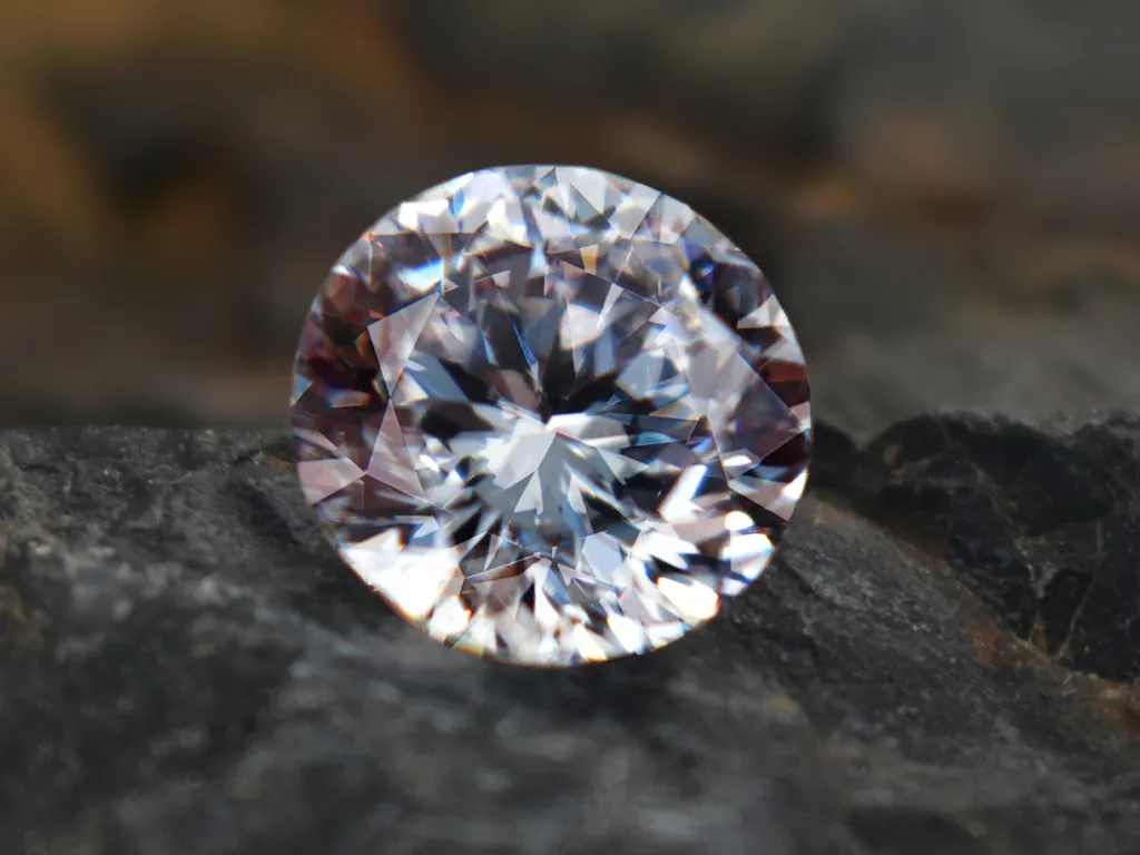 Sparkling round diamond resting on dark stone, showcasing its brilliance.