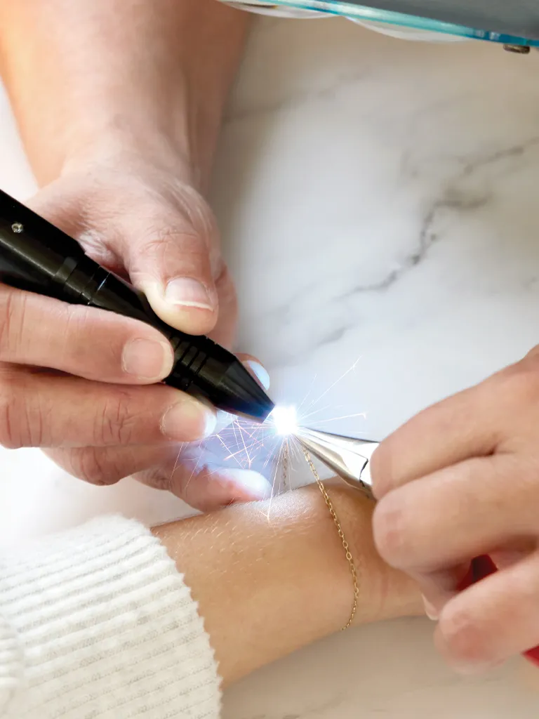 A jeweler uses a light tool to work on a delicate bracelet on a client's wrist