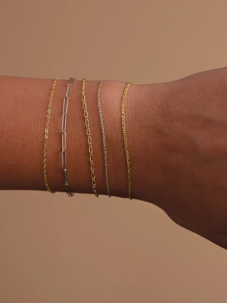 Delicate gold and silver chain bracelets worn on a wrist against a neutral background.