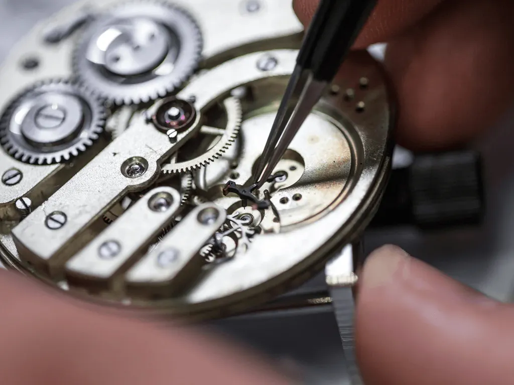 A watchmaker carefully repairs a watch movement using tweezers, showcasing intricate gears and components.