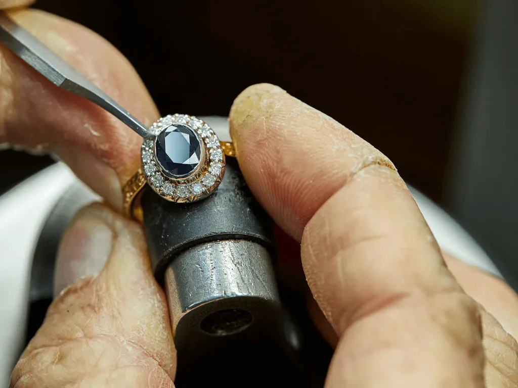 Jeweler setting a sapphire ring with diamonds, showcasing craftsmanship.