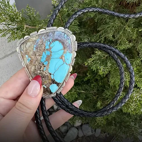 Turquoise bolo tie with silver accents, held against greenery.