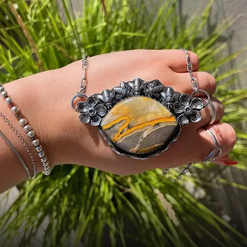 Hand holding a floral silver necklace with a large, colorful stone. Click to Shop Now at Michael & Son's Jewelers.