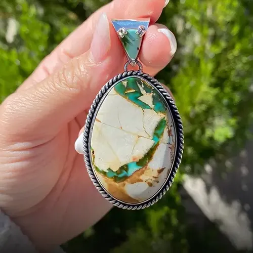 Turquoise and brown pendant held in hand, featuring intricate patterns and silver detailing.