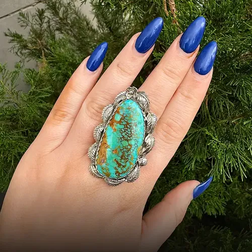 Turquoise ring with silver detailing on a hand with long blue nails.