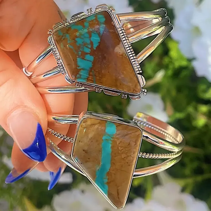 Two stunning turquoise and brown stone bracelets in silver settings, held in a hand with blue nails.