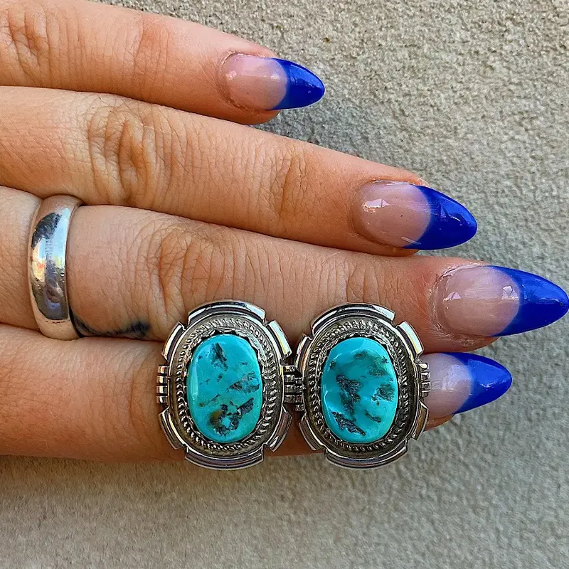 Turquoise Sleeping Beauty earrings set in silver, displayed on a hand with stylish blue-tipped nails.