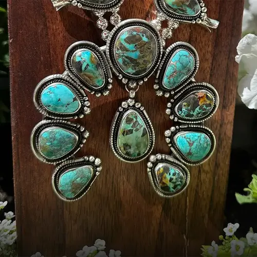 Turquoise squash blossom necklace with silver accents displayed on a wooden background.
