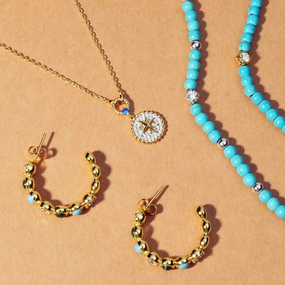 Gold jewelry set featuring a compass pendant necklace, turquoise beaded necklace, and gold hoop earrings.