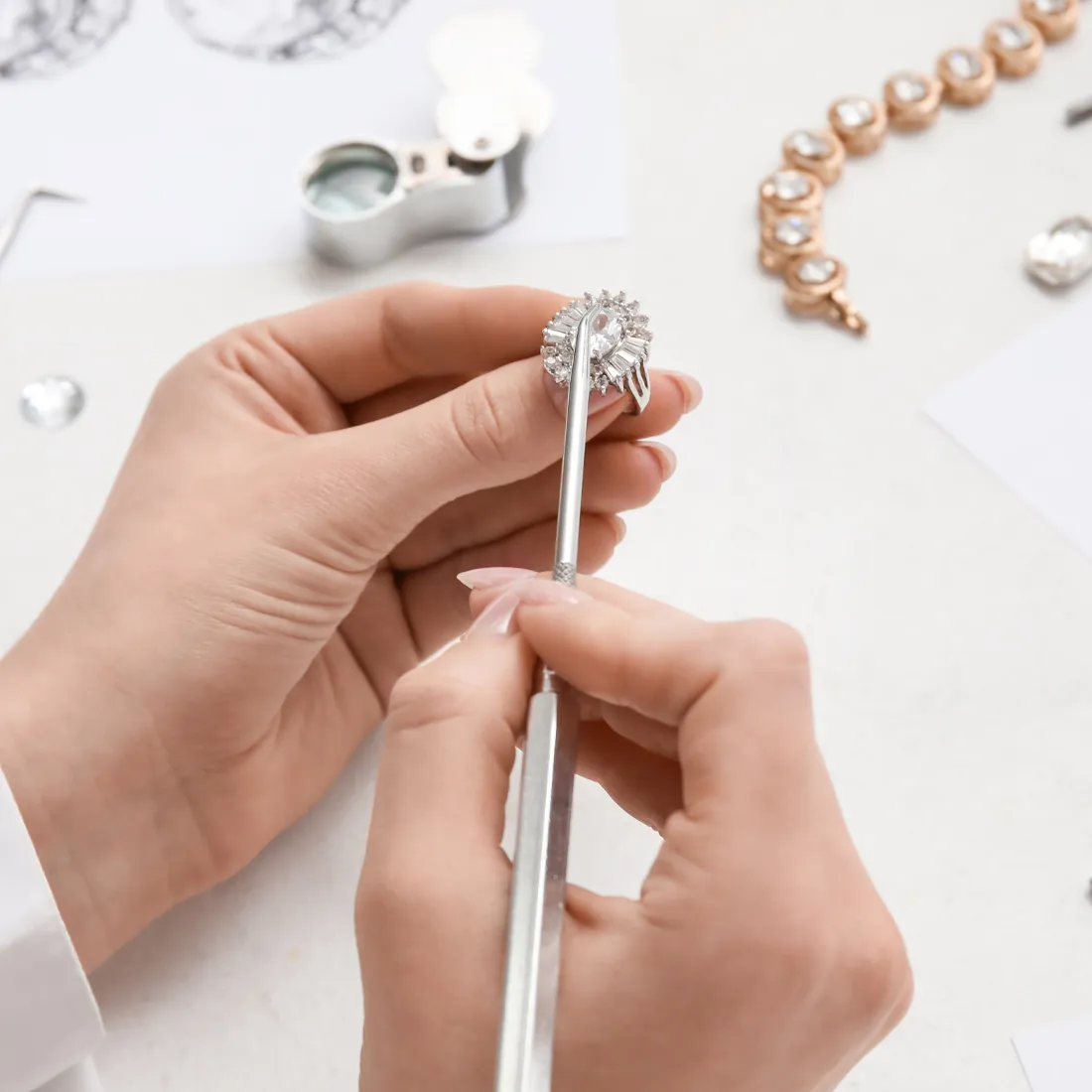 A jeweler carefully inspects a diamond ring using a tool, surrounded by jewelry-making materials.