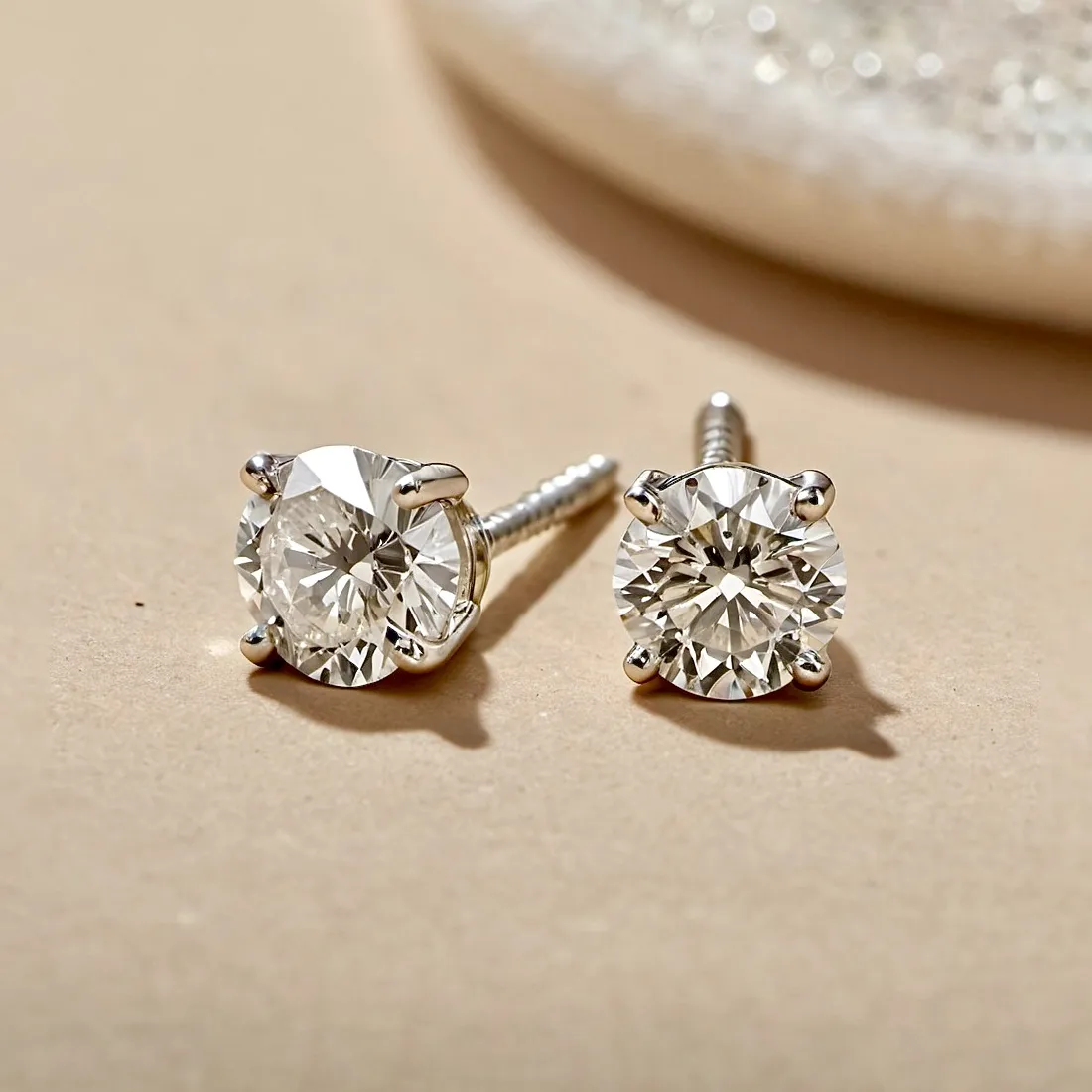 Close-up of diamond stud earrings on a beige background, showcasing their brilliance and setting.