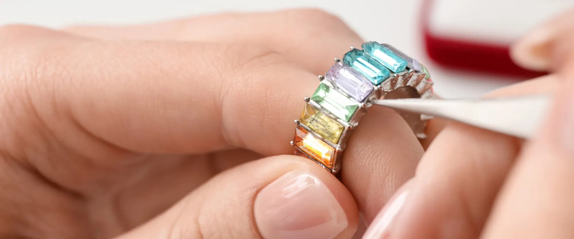A jeweler carefully adjusts a colorful gemstone ring with tweezers, showcasing vibrant stones in a silver setting. 