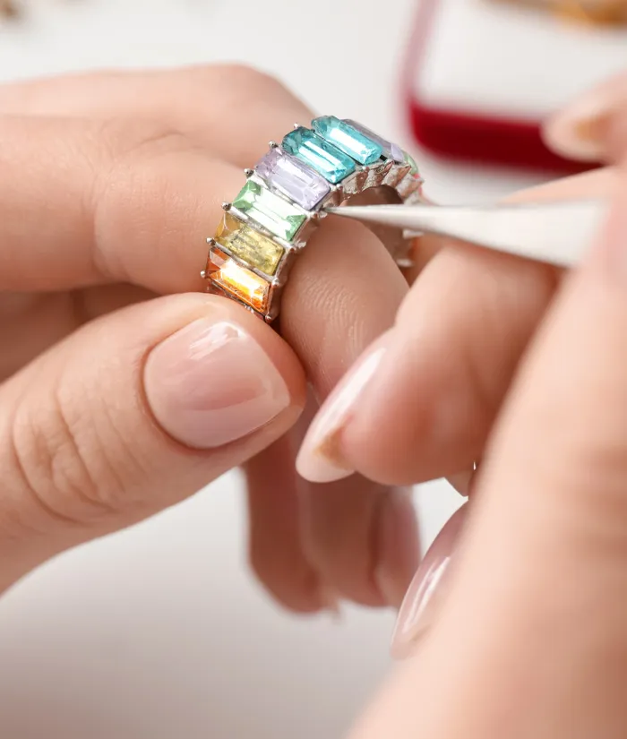 A jeweler carefully adjusts a colorful gemstone ring with tweezers, showcasing vibrant stones in a silver setting. 