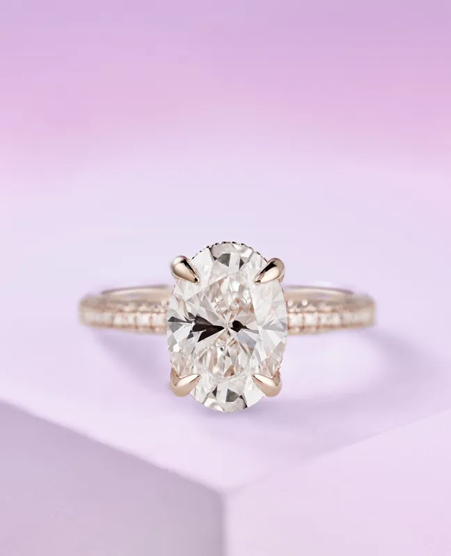 Oval diamond engagement ring with a rose gold band, displayed on a soft purple background.