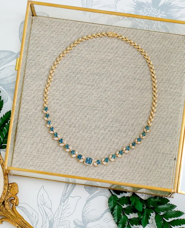 Gold necklace with blue gemstones displayed on a textured background. 