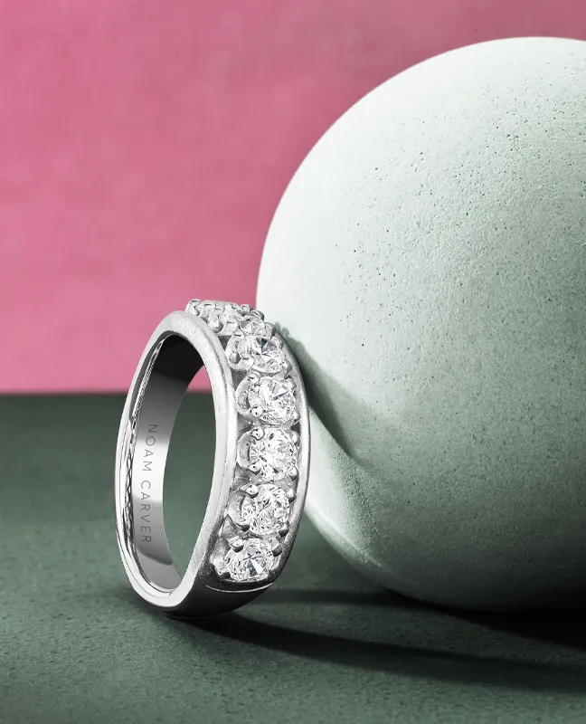 Elegant diamond wedding band by Noam Carver, displayed beside a smooth green sphere.