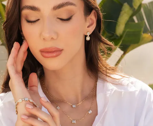 Gold layered necklaces with a emerald cut diamonds and delicate chain worn by a smiling woman in a white shirt.