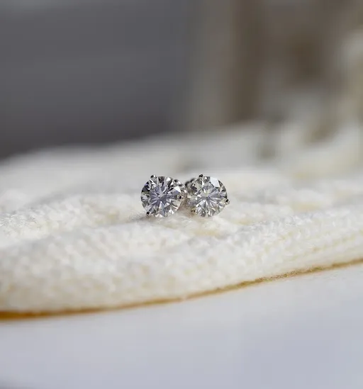 A pair of round lab-grown diamond stud earrings resting on cream knit