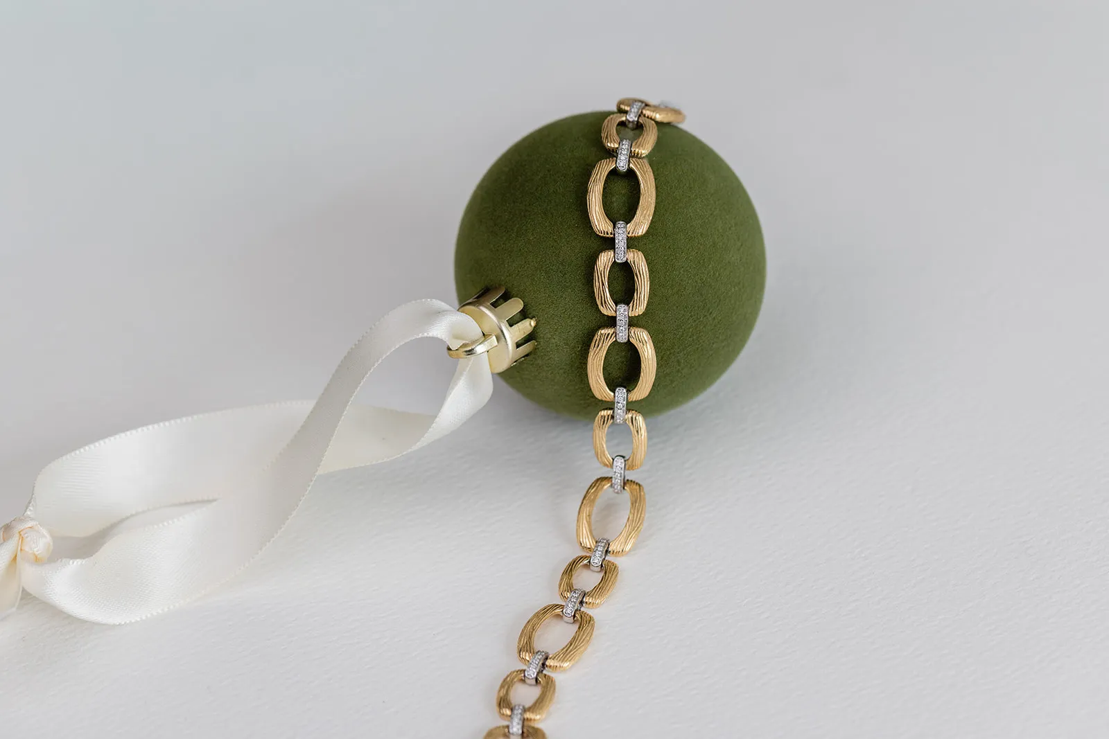 Gold link bracelet draped over a green velvet ornament with ivory ribbon
