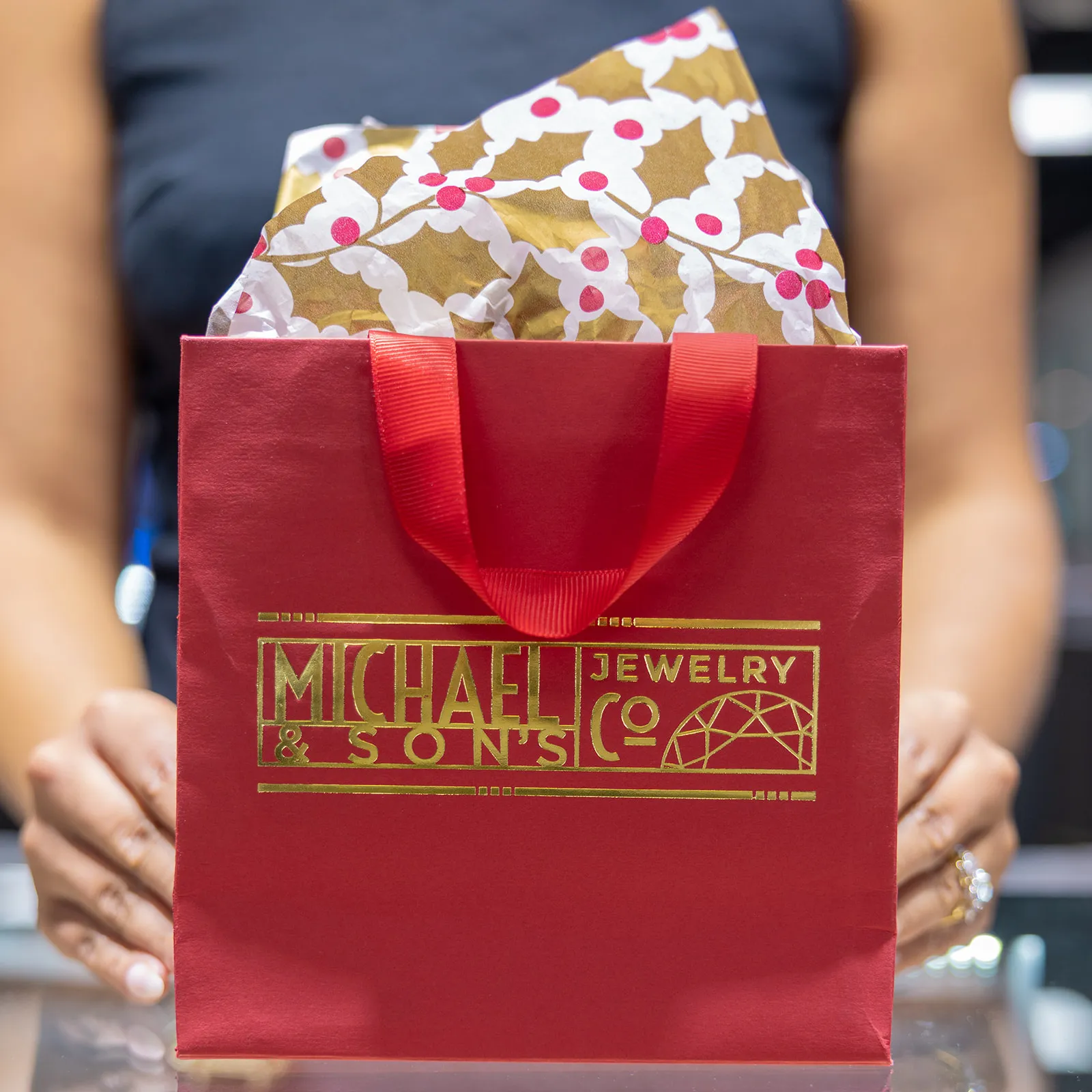 A Michael & Son's team member holding a red holiday gift bag