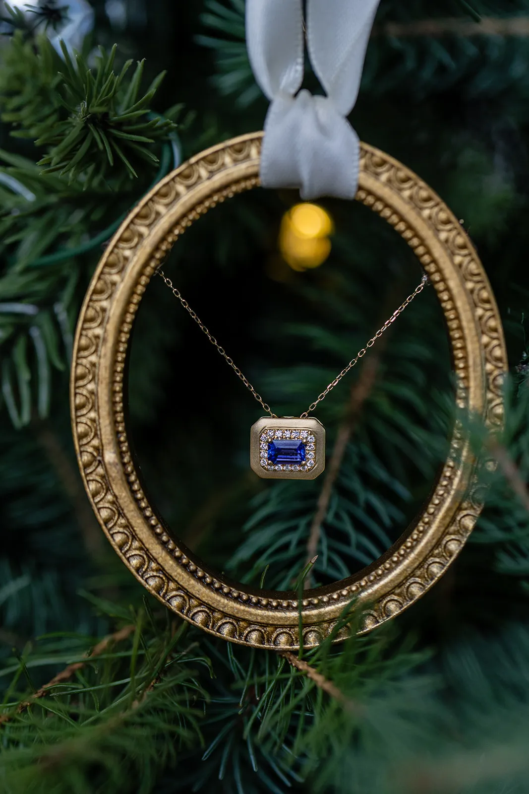 Sapphire and diamond pendant hanging in a gold oval frame on a Christmas tree